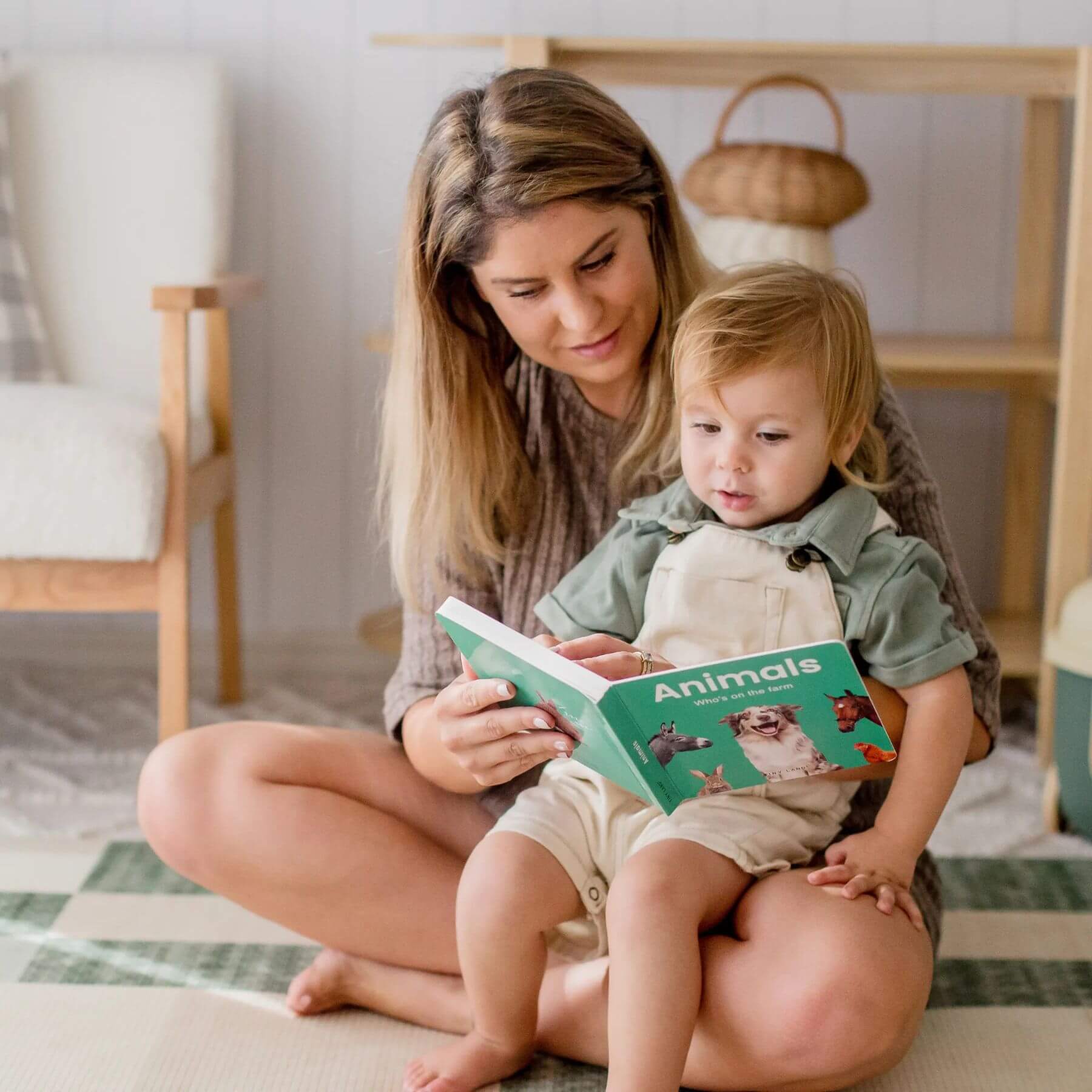 Woman reading a book titled 'Animals' to a child in a cozy room.