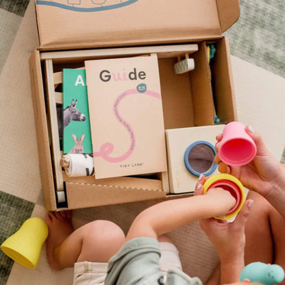 Child playing with colorful cups next to an open box containing educational materials