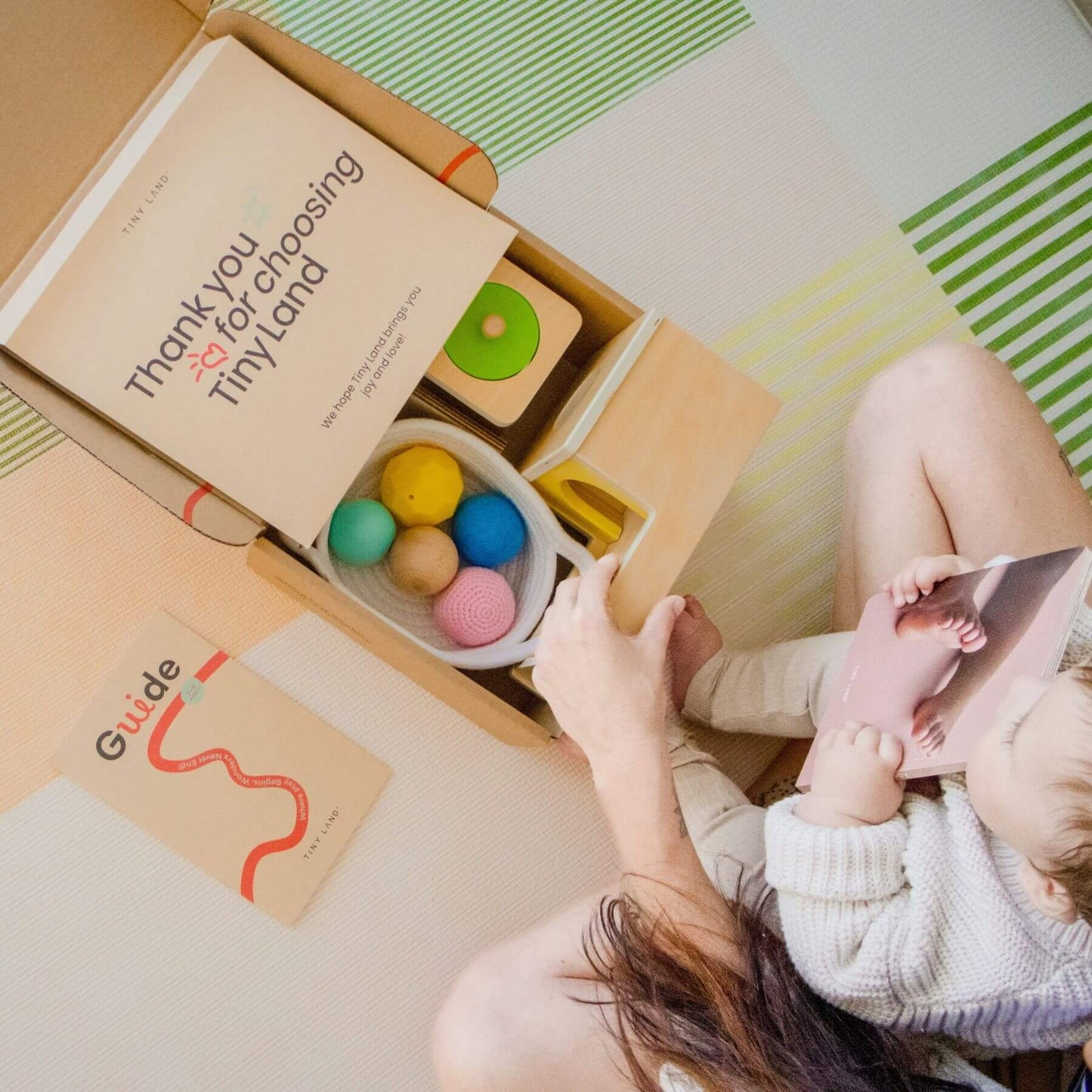 Child playing with colorful toys from a Tiny Land box on a patterned floor.
