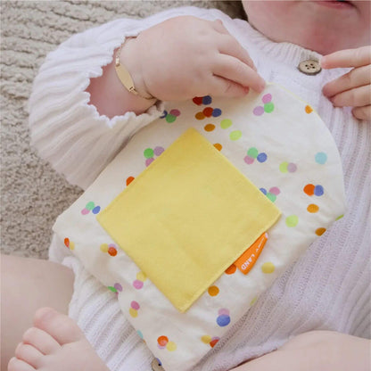 Baby holding a colorful polka dot blanket with a yellow square