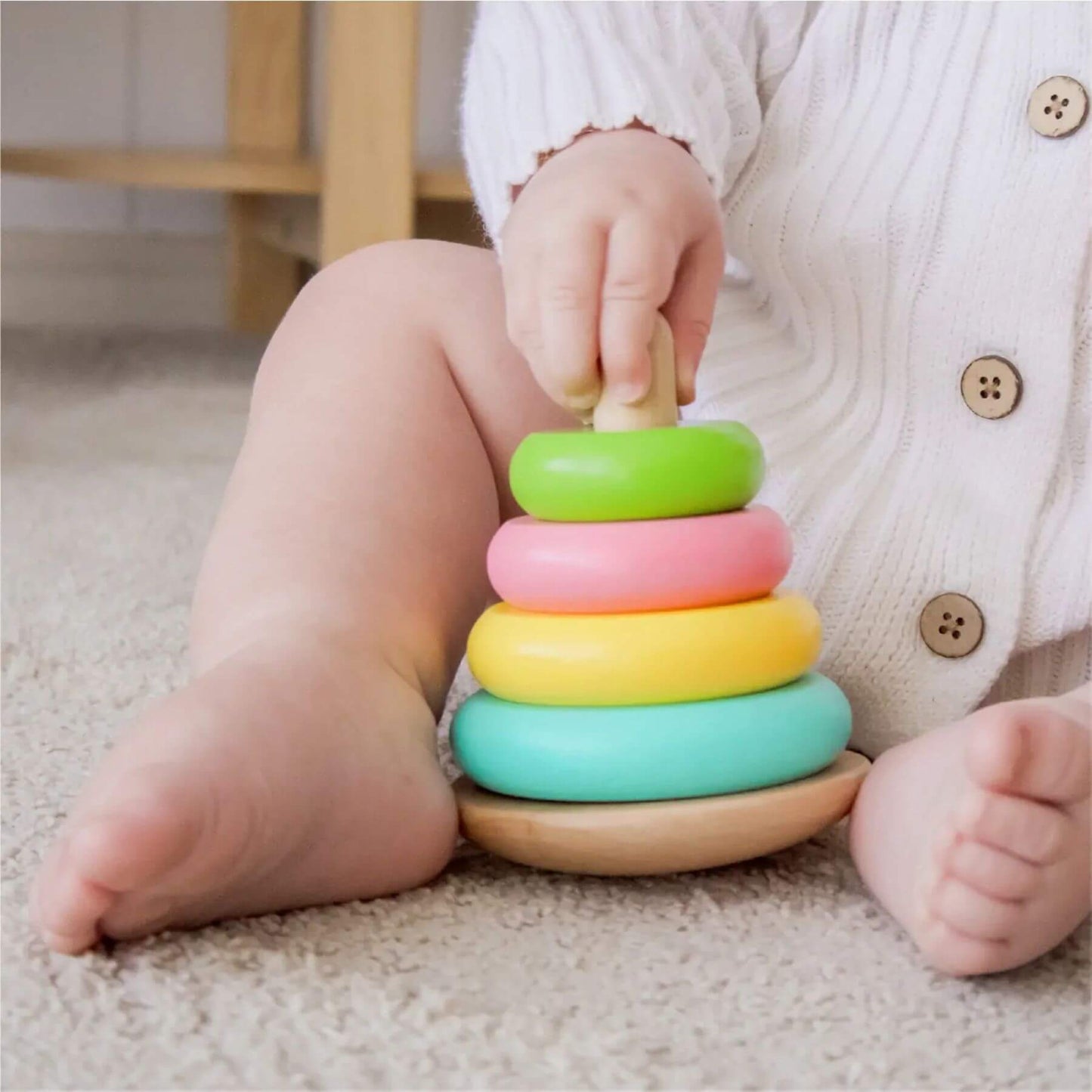 Child playing with a colorful wooden stacking toy on a carpeted floor.