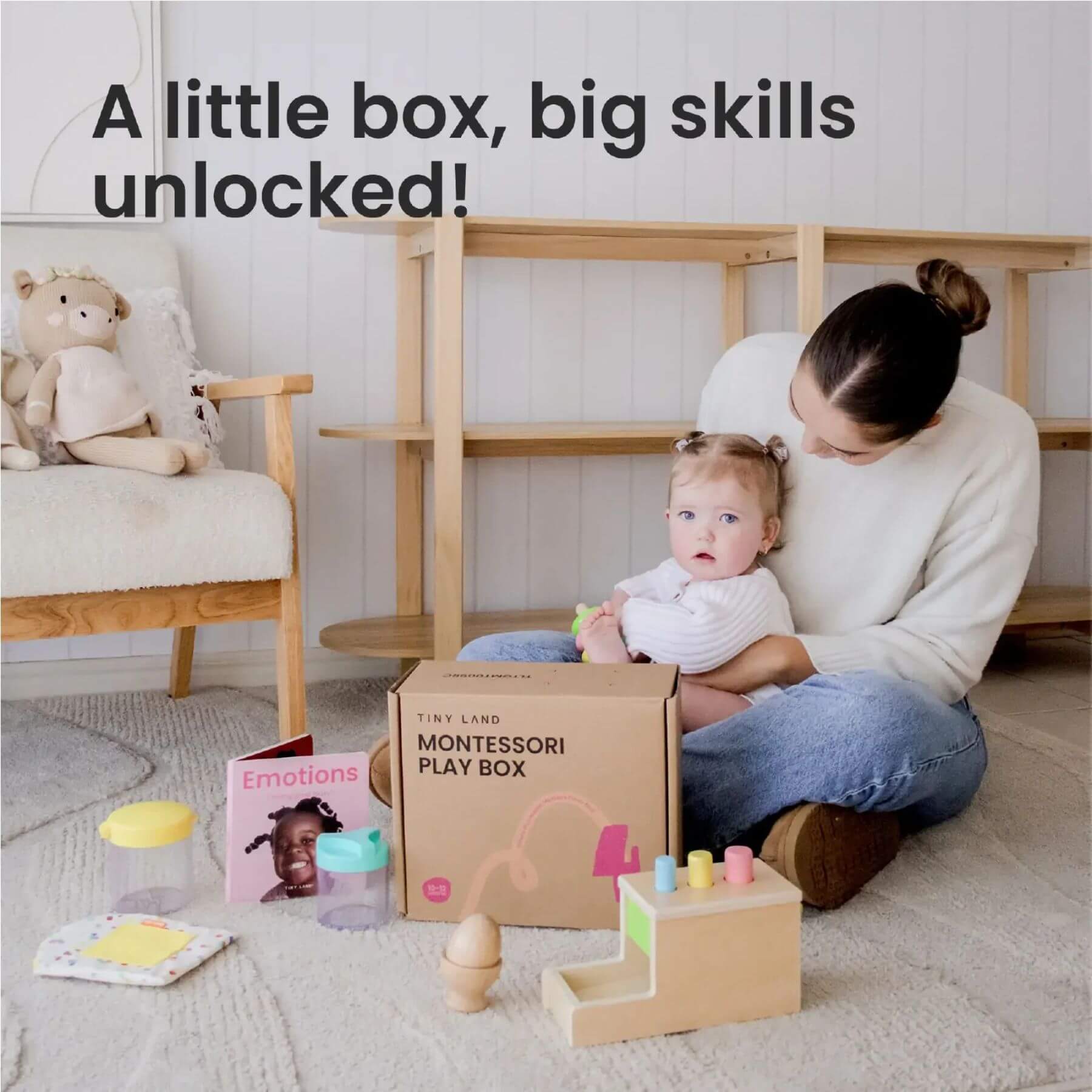 Woman holding a baby with Montessori play items and a box labeled 'Montessori Play Box' in a home setting.