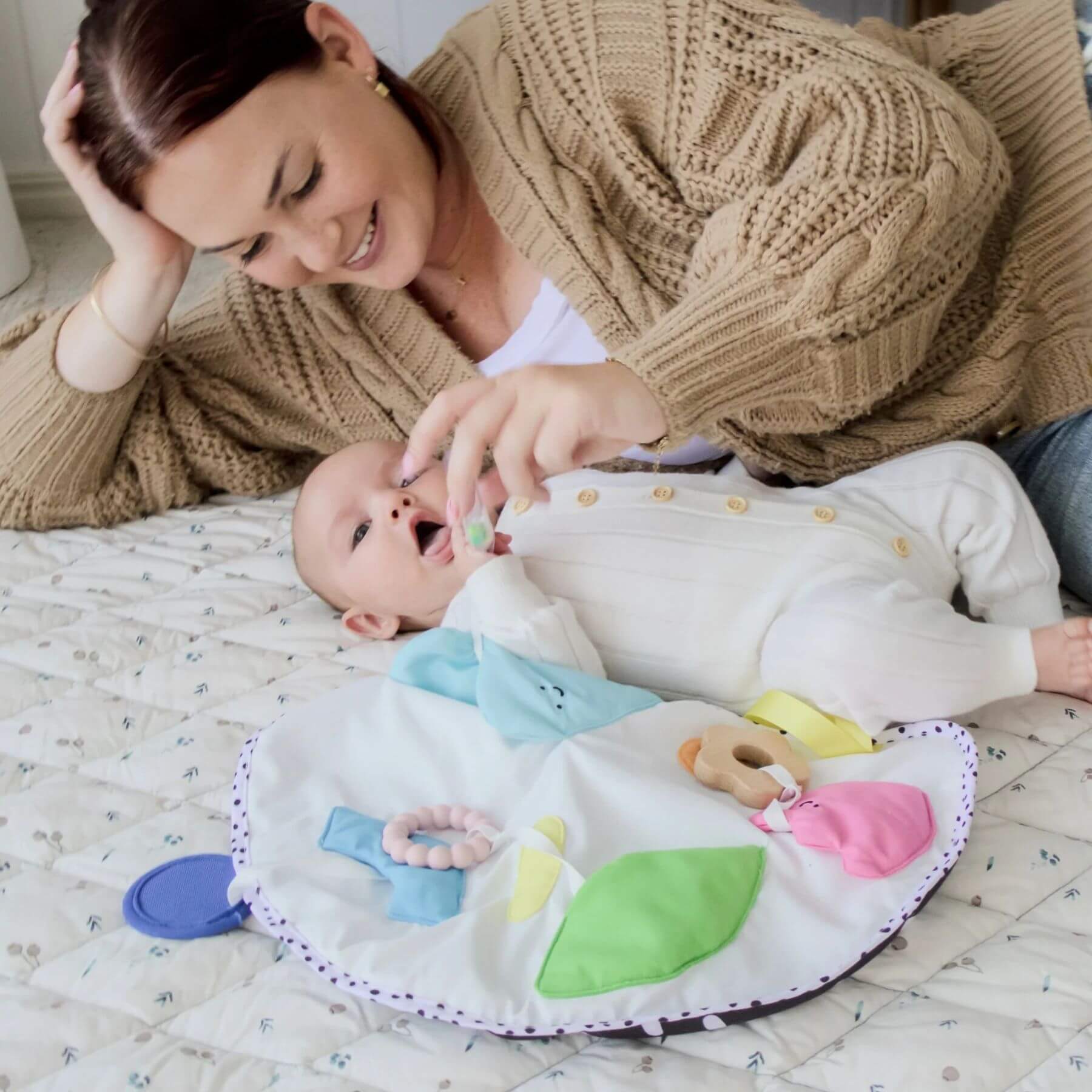Woman lying on a bed with a baby and a colorful play mat