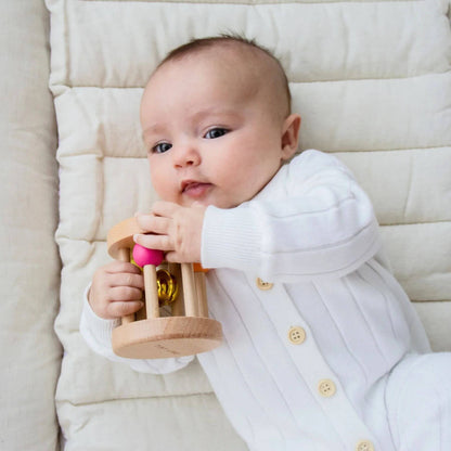 Baby holding a wooden rattle on a soft surface