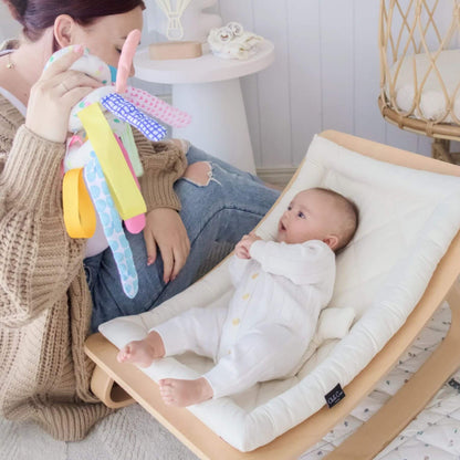 Baby in a rocker with a woman holding a colorful toy