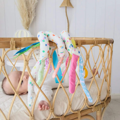 Baby lying in a crib with colorful tassels hanging over the side