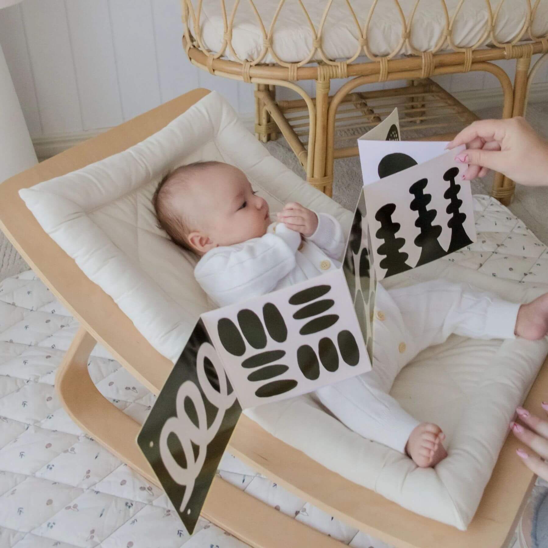 Baby lying on a wooden crib with a person holding a black and white card.