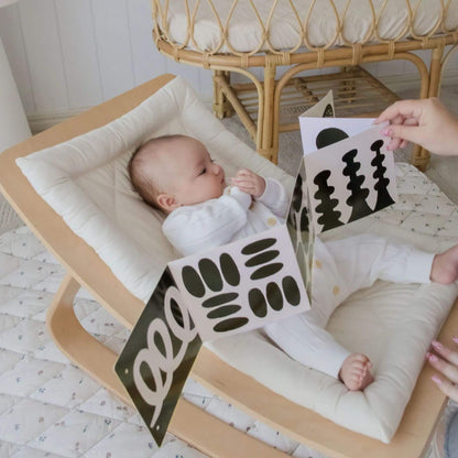 Baby lying on a wooden crib with a person holding a black and white card.
