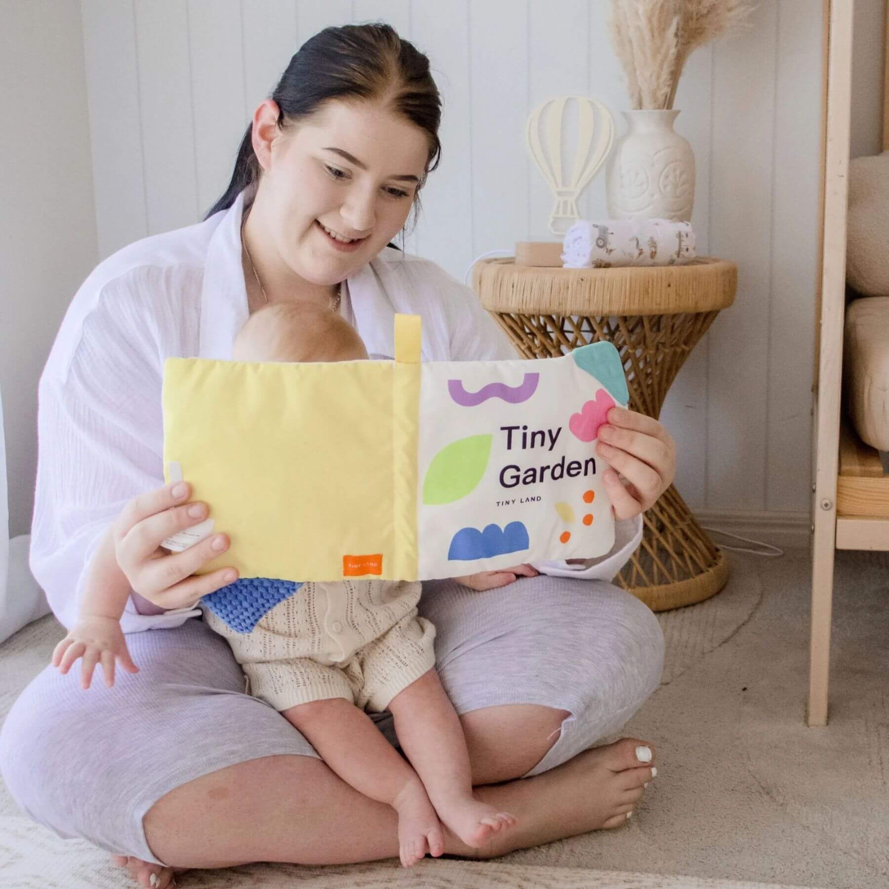 Woman reading a children's book to a baby in a cozy room.