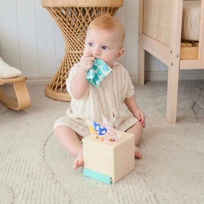 Baby sitting on a carpeted floor with a wooden toy and colorful bandana