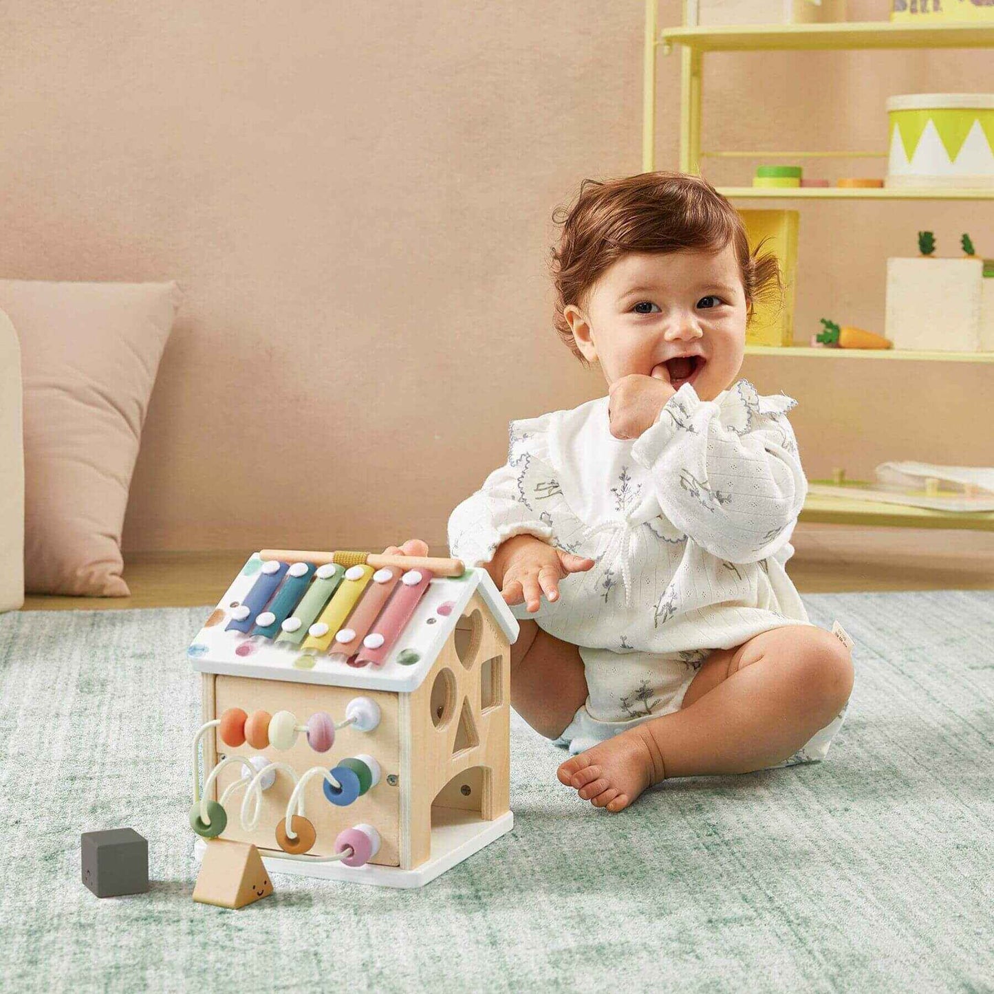 Baby playing with Tiny Land® Cottage Activity Cube - Morandi in a room with a beige wall and shelves.