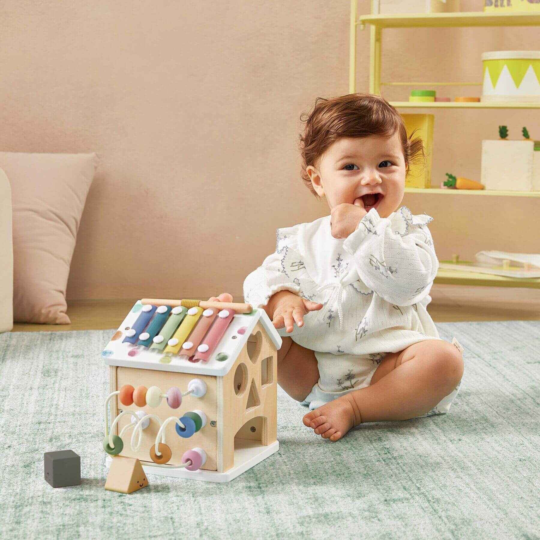 Baby playing with Tiny Land® Cottage Activity Cube - Morandi in a room with a beige wall and shelves.