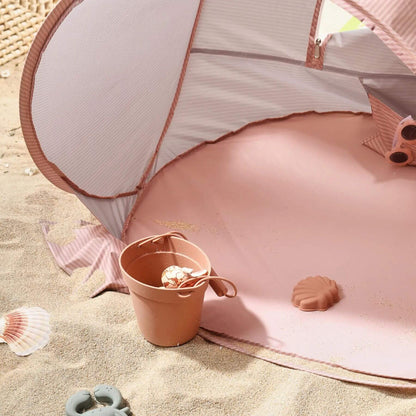 Pink beach tent with sand toys on a sandy surface