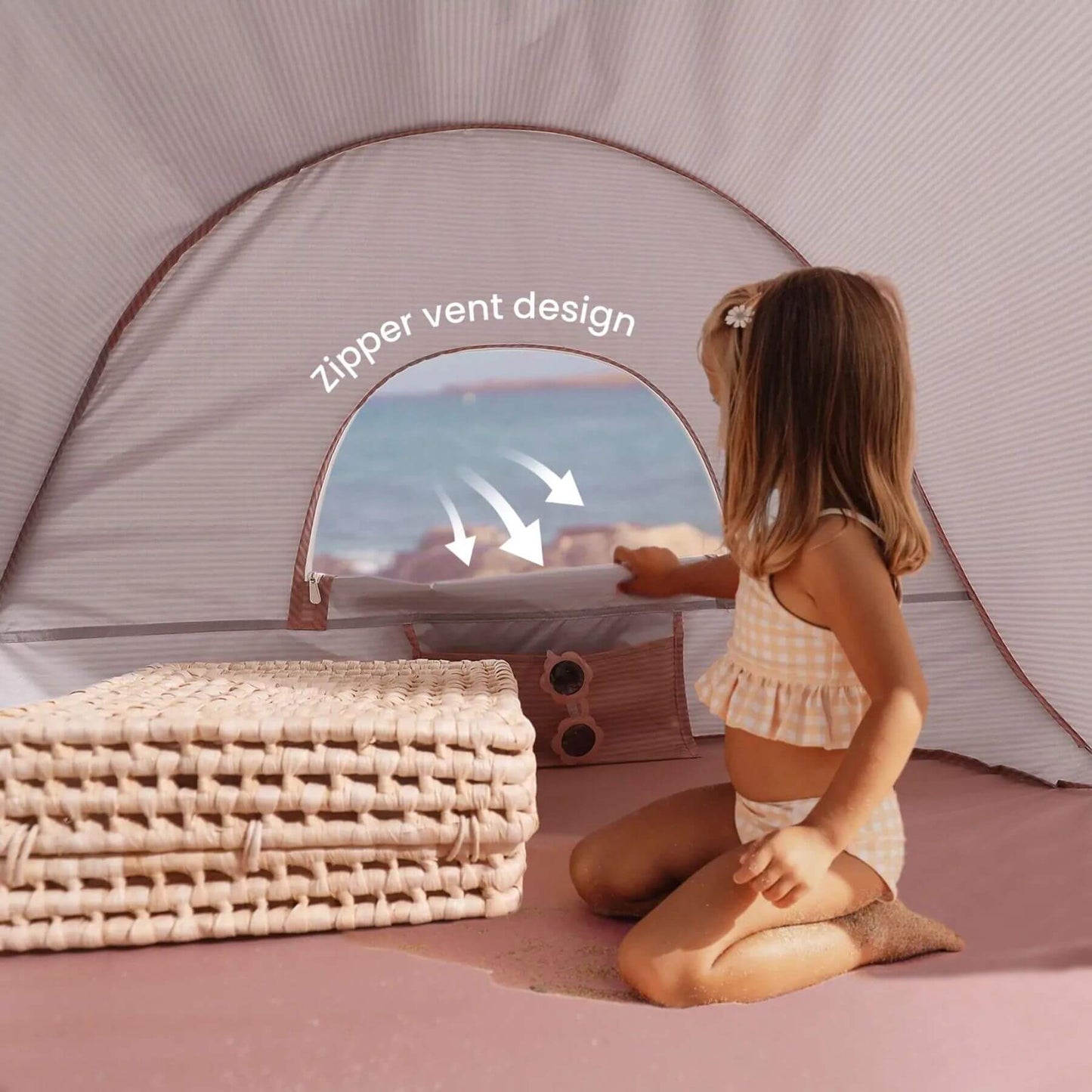 Child looking outside a tent with a zipper vent design, sitting on a pink surface.