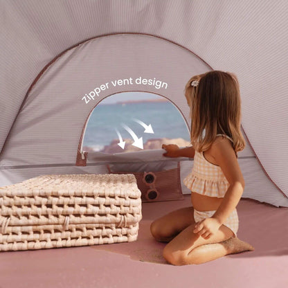 Child looking outside a tent with a zipper vent design, sitting on a pink surface.