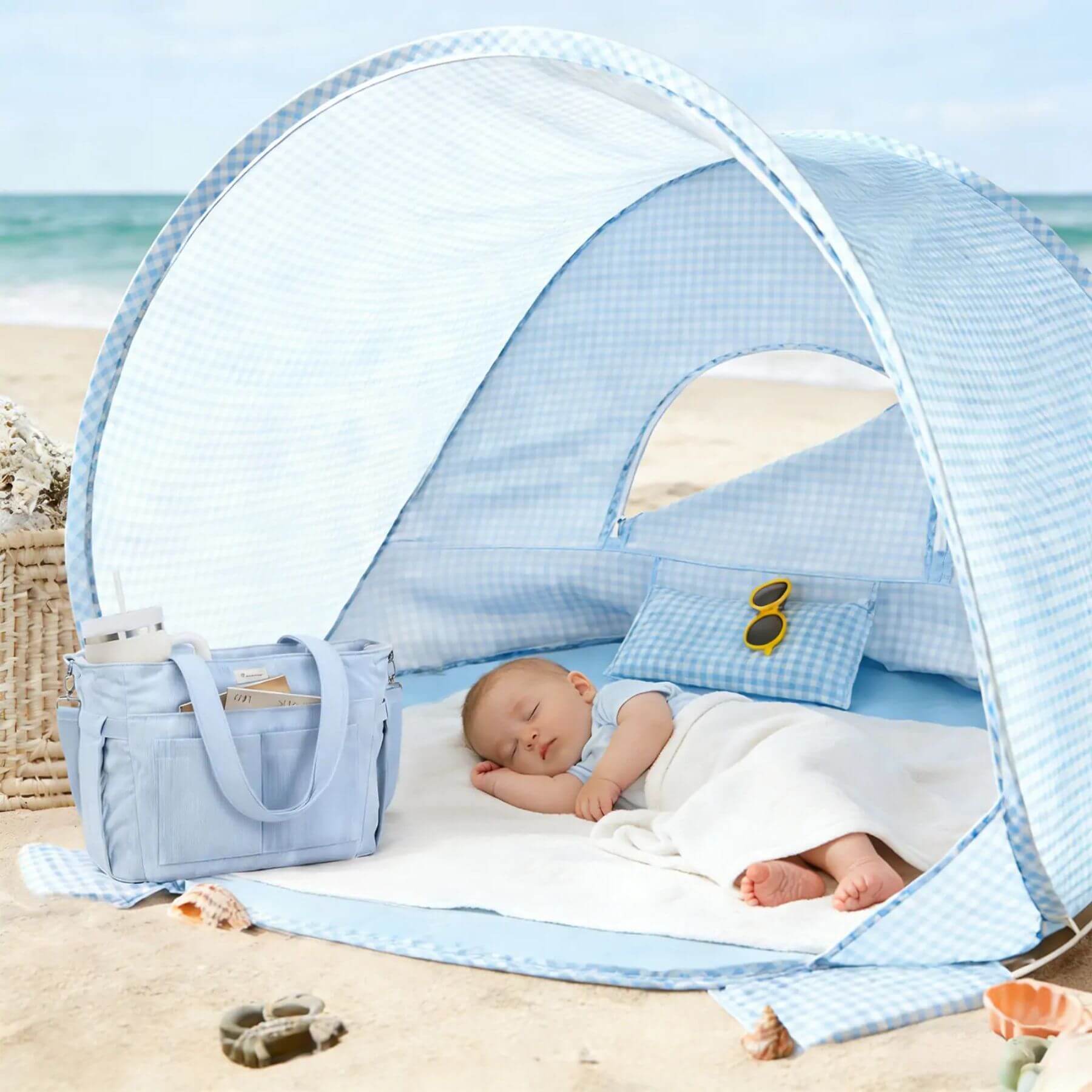 Baby sleeping in a blue baby beach tent on a sandy beach with ocean view
