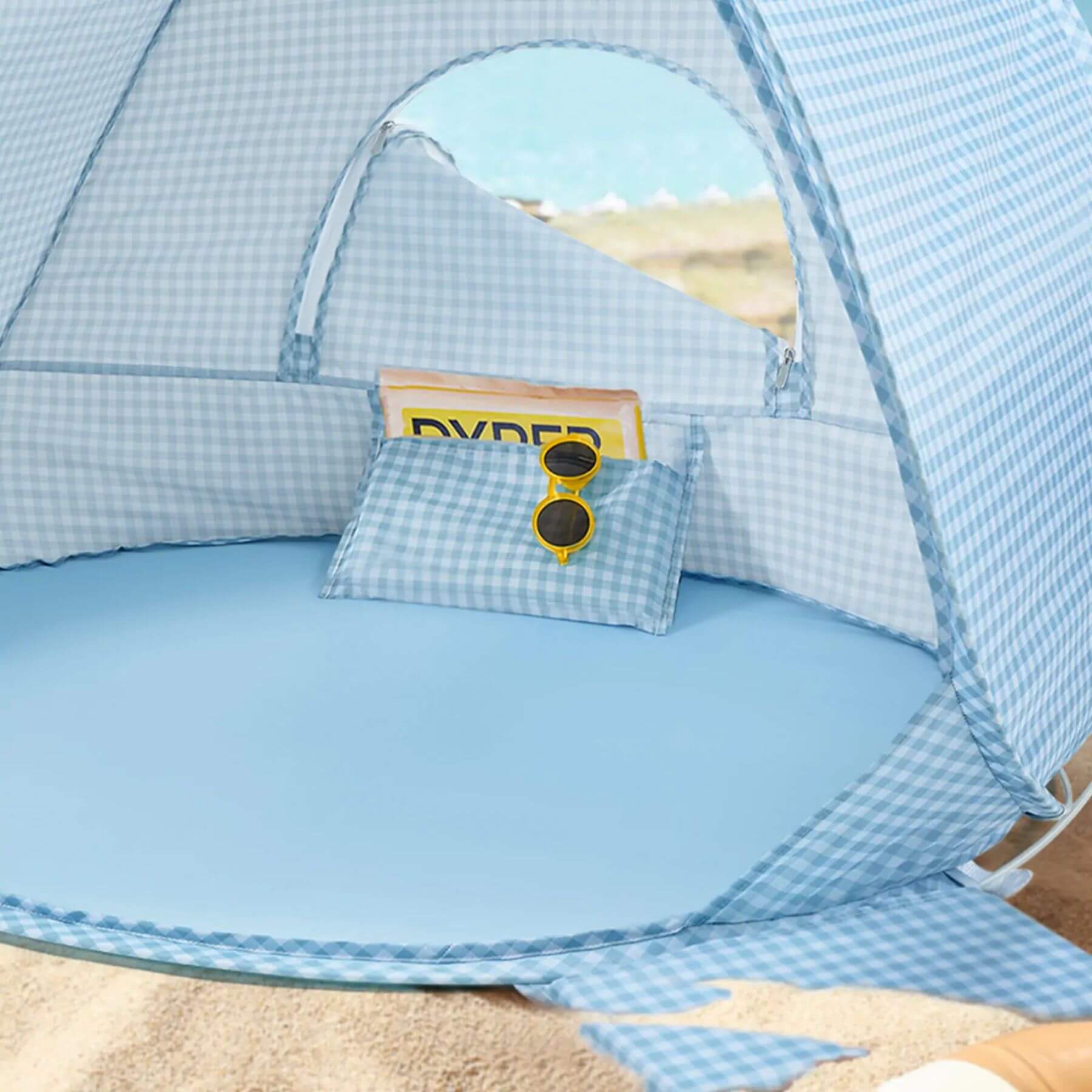 Blue baby tent with a small bag and sunglasses on a sandy background