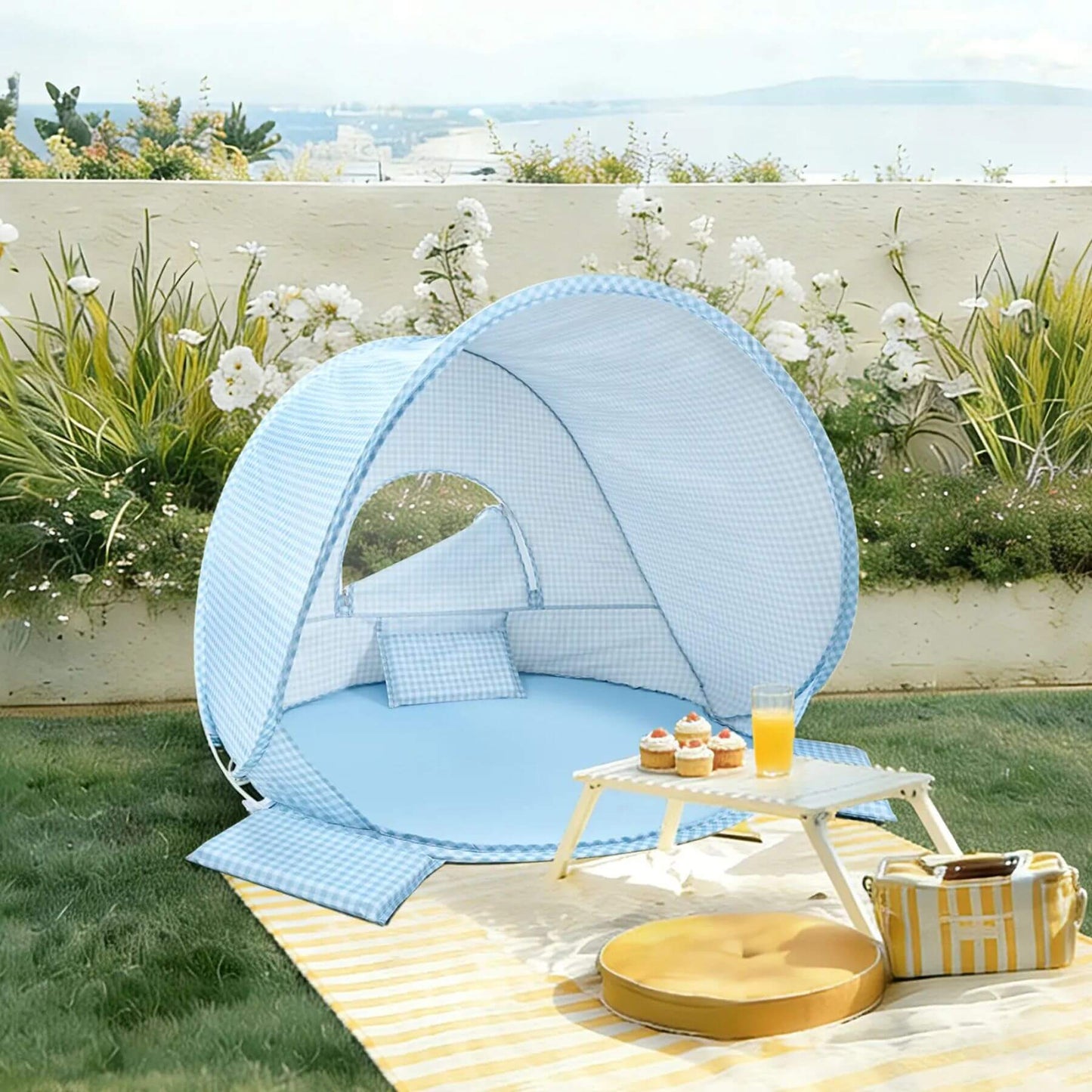 Portable outdoor canopy with pillows and a small table on a grassy area with flowers and plants.