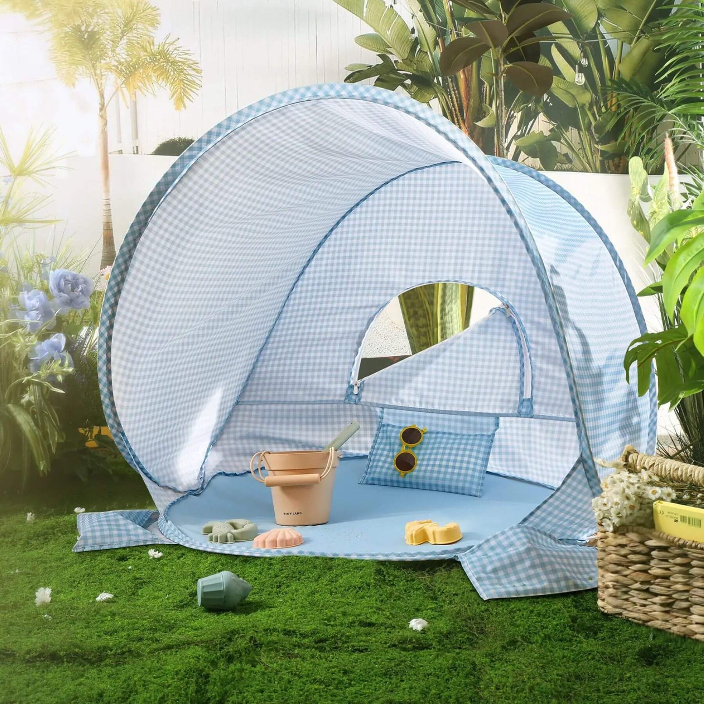 Blue checkered beach tent with accessories on a grassy area with plants and flowers in the background