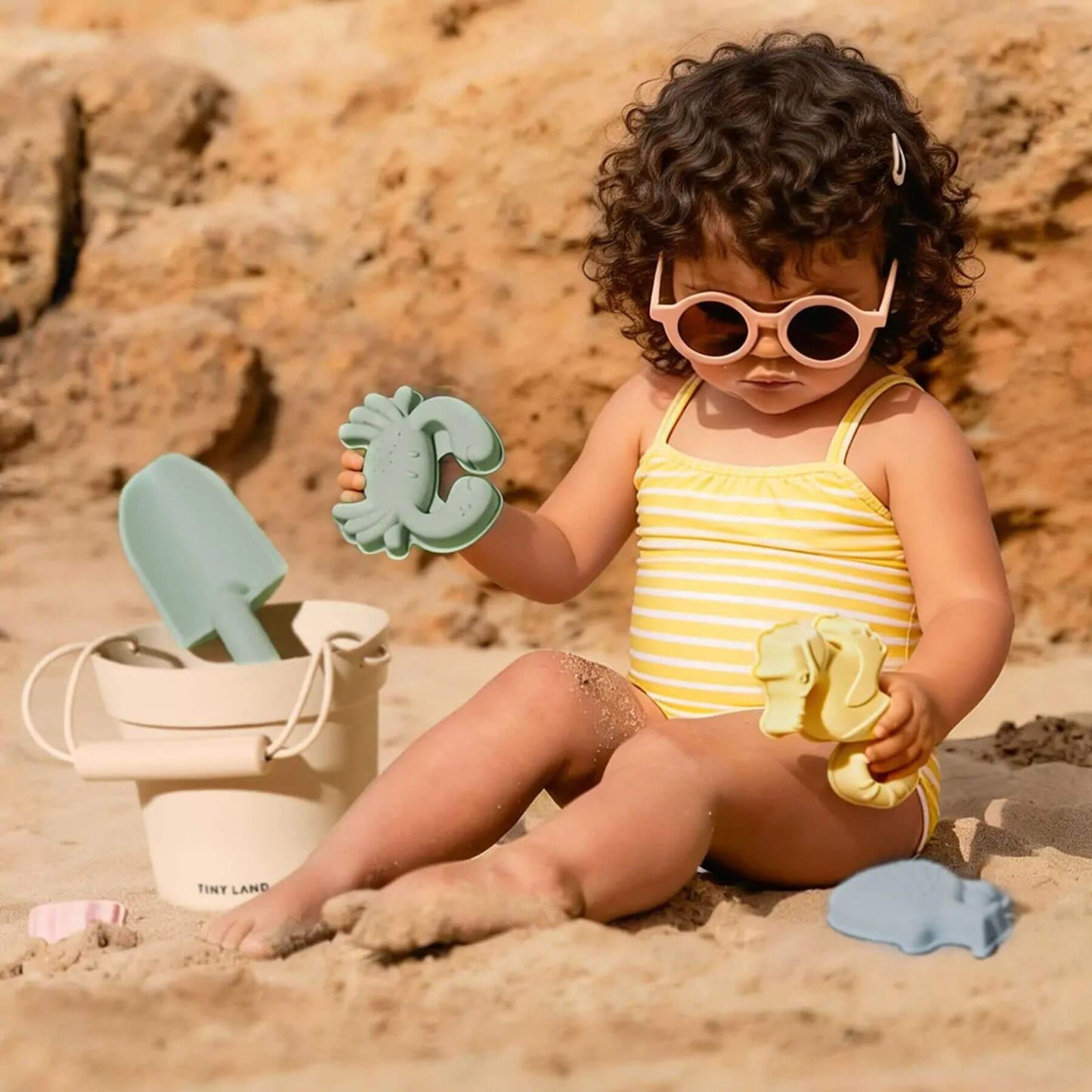 Child playing on a beach with sand toys and sunglasses