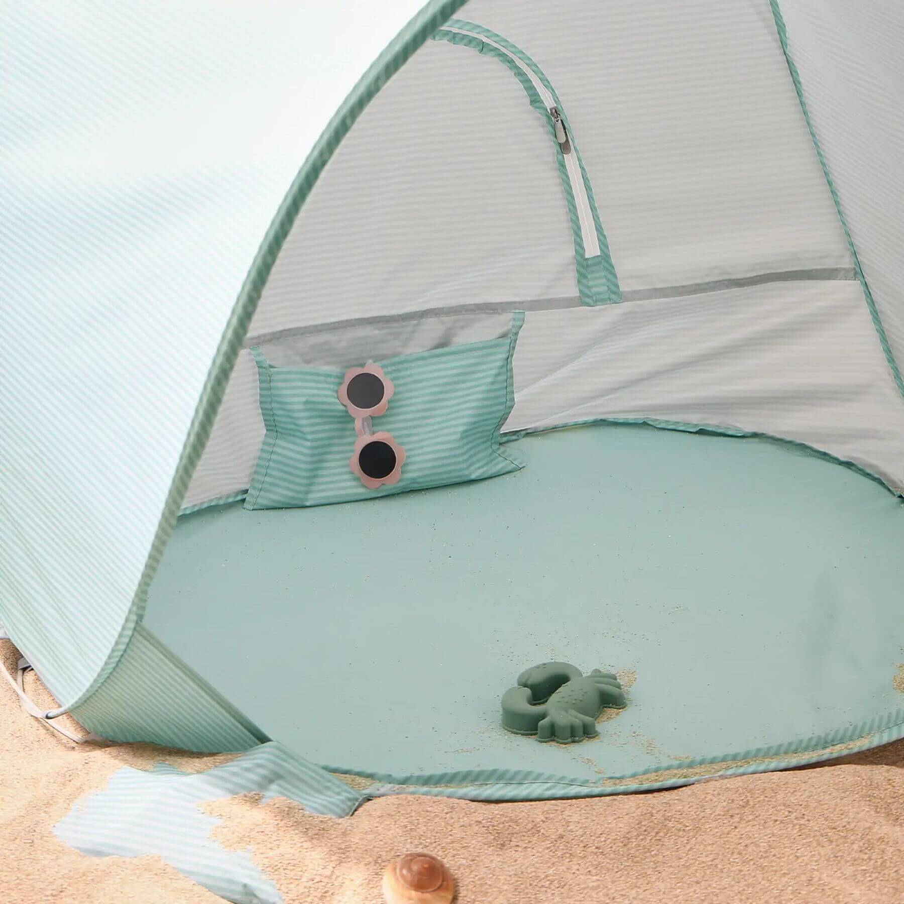 Light blue baby tent with sunglasses and a toy on a sandy surface