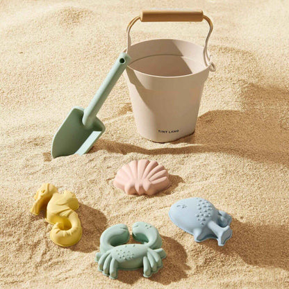 Children's sand toys including a bucket, shovels, and molds on a sandy surface.