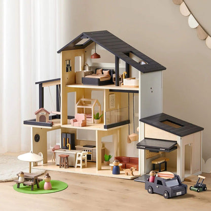 A large wooden dollhouse with an open roof and multiple interior rooms, shown on a light wood floor against a soft beige wall. The dollhouse includes a bedroom, kitchen, living area, garage, and small accessories like miniature furniture and toy vehicles.