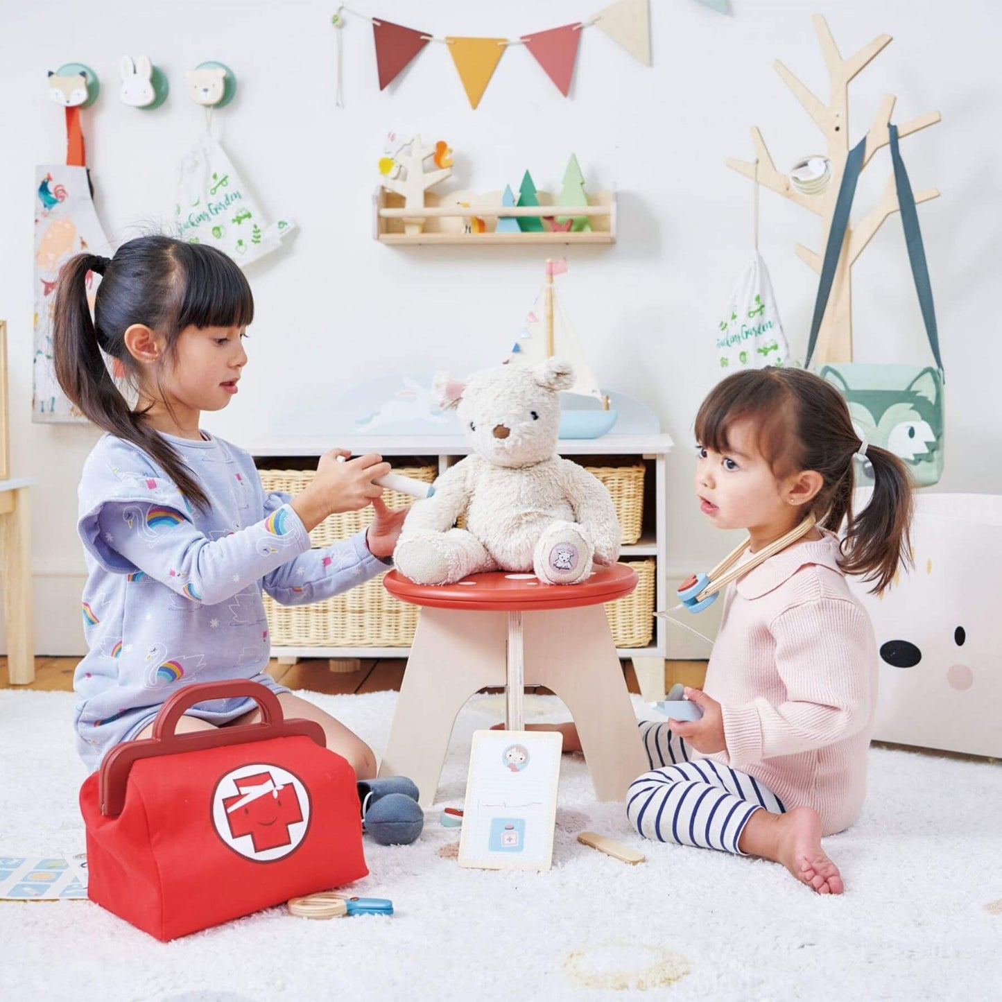 Two children playing with a teddy bear in a child-friendly room with toys and decorations.