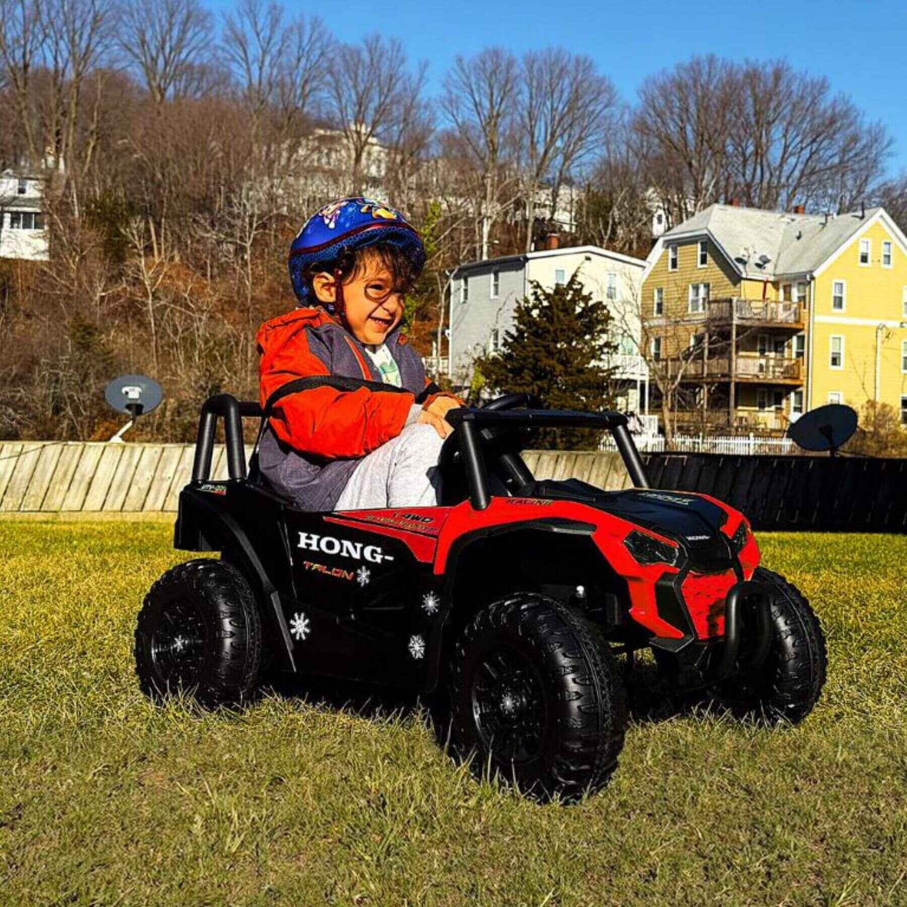 Child sitting in Tamco 12V Ride On UTV Toy Electric Car - Red on grass with houses in the background