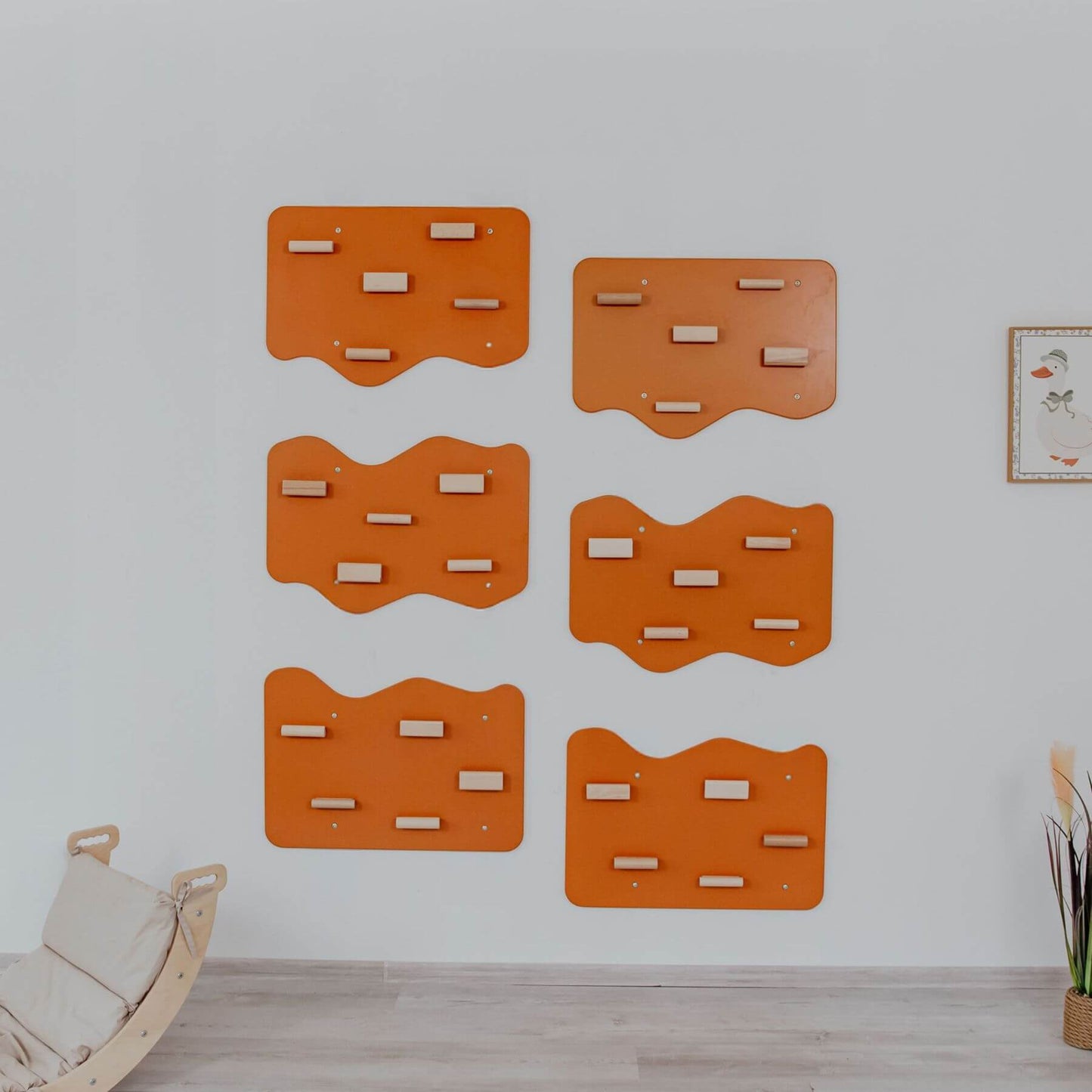 Set of orange wall-mounted climbers on a white wall with a wooden floor and plant in the corner.
