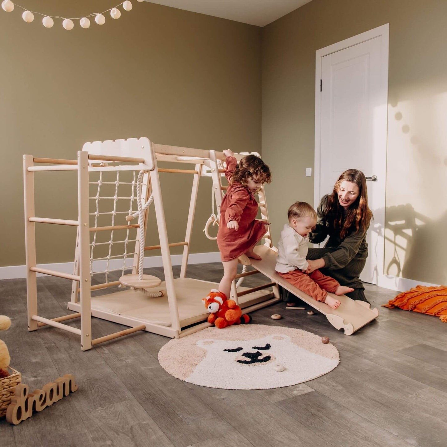 Children playing on Wood and Hearts Jungle Gym Playset in a room with a woman supervising.