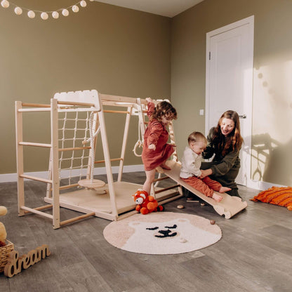 Children playing on Wood and Hearts Jungle Gym Playset in a room with a woman supervising.