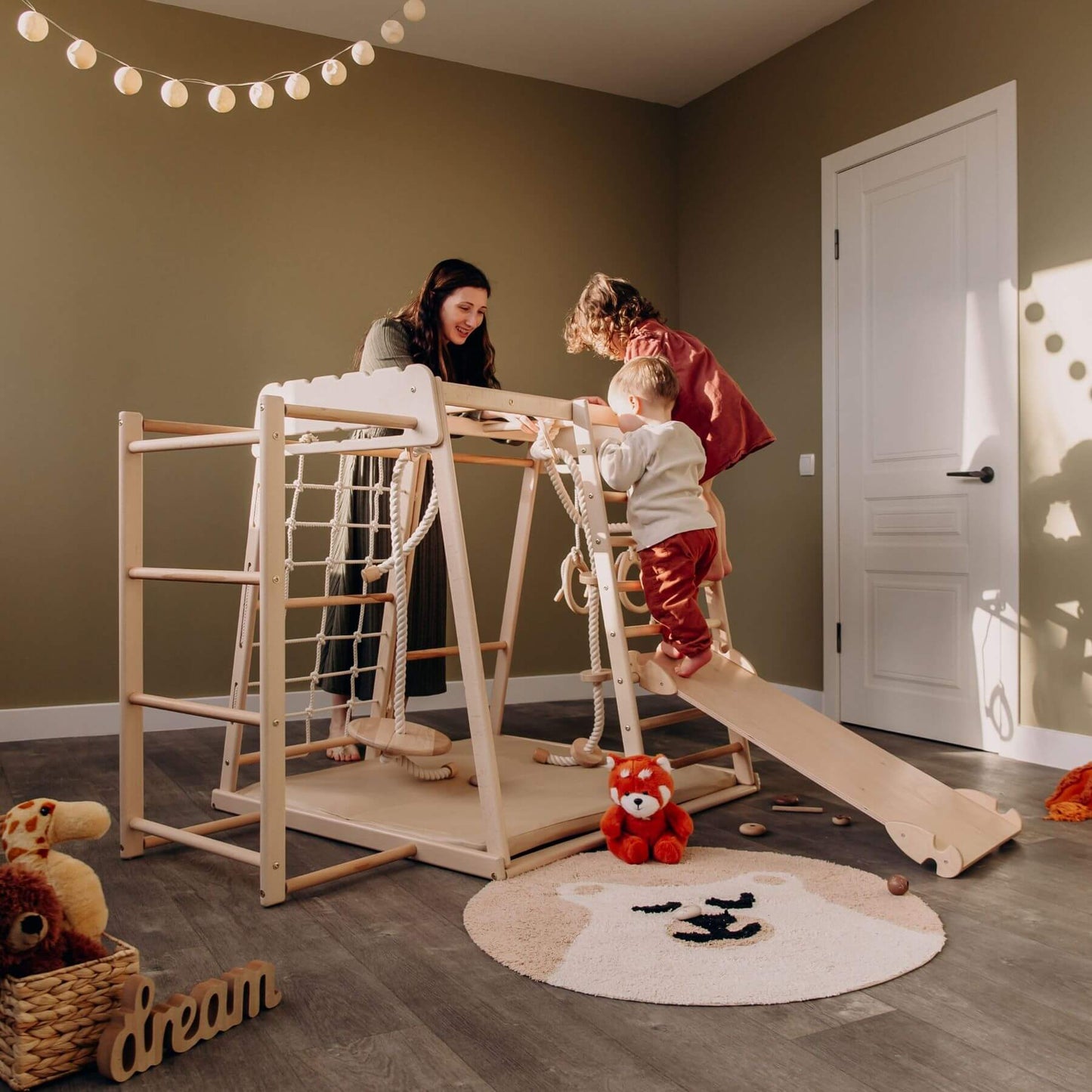 Children playing with Wood and Hearts Jungle Gym Playset in a room with a brown wall and white door.
