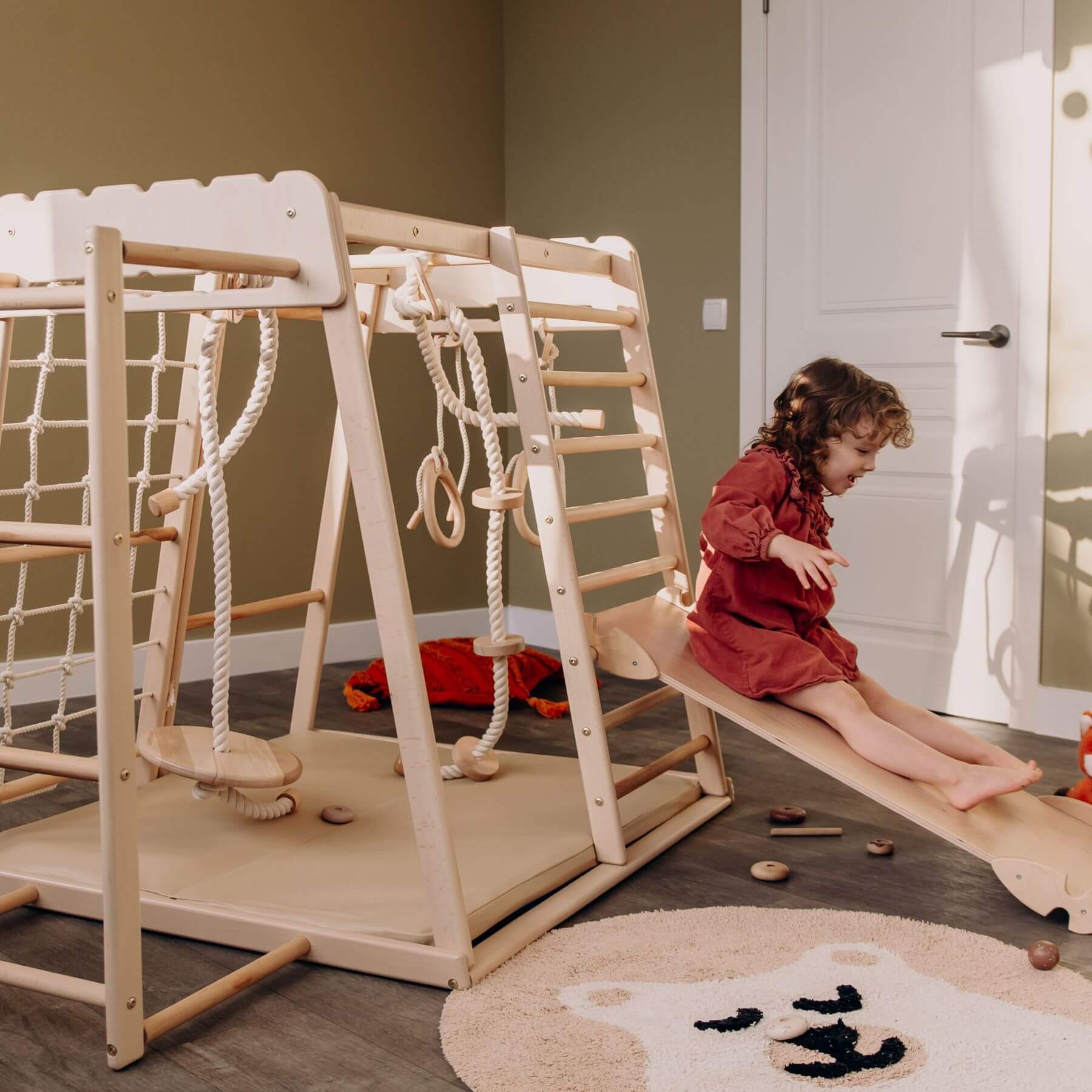 Child playing on Wood and Hearts Jungle Gym Playset in a room with a rug and toys.