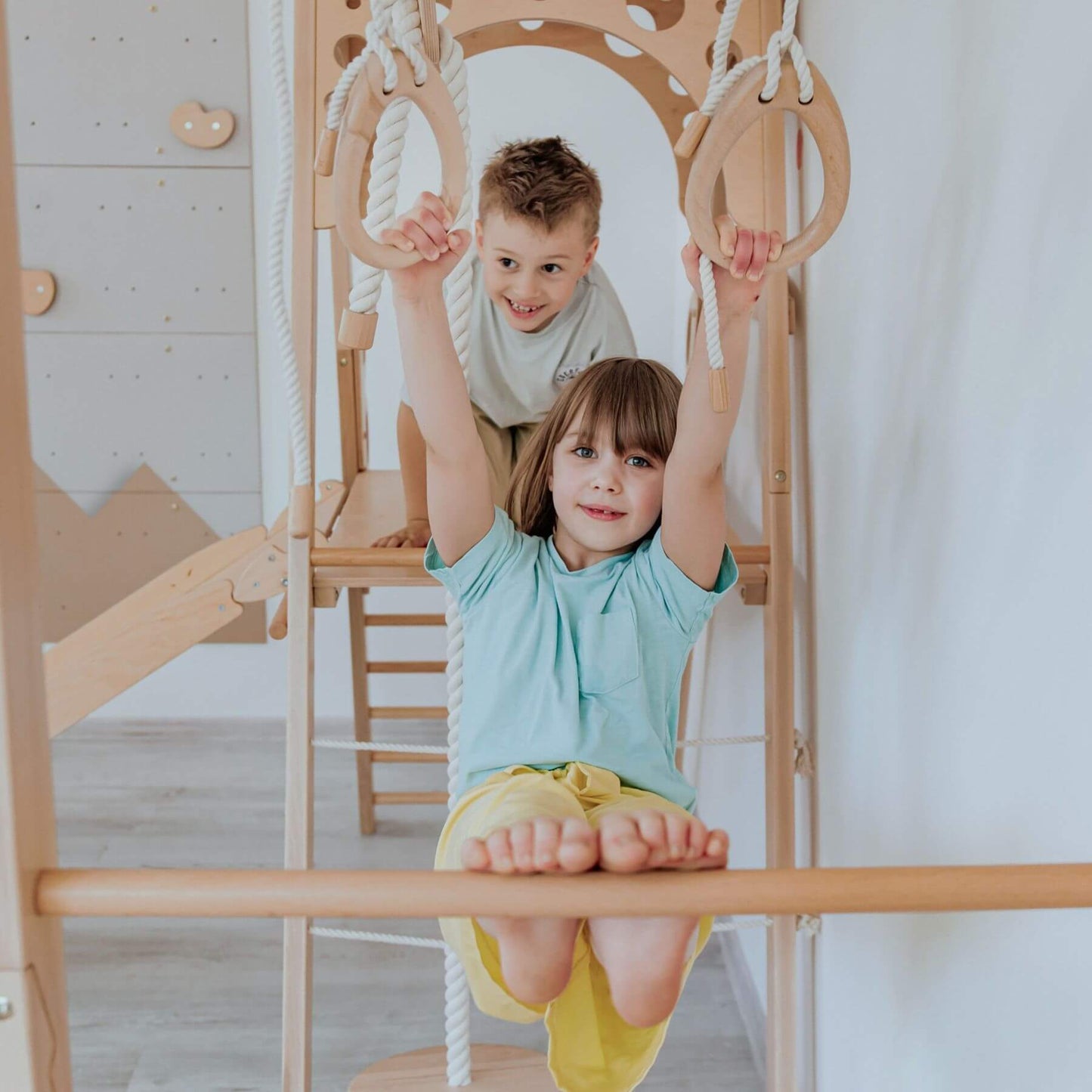 Two children playing on a wooden climbing frame indoors.
