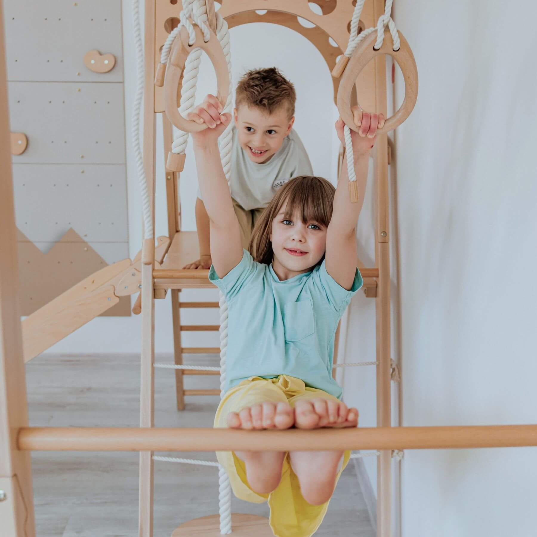 Two children playing on a wooden climbing frame indoors.