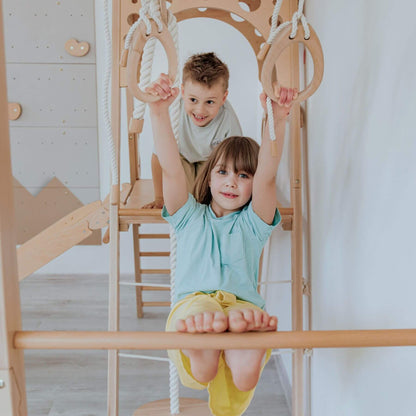 Two children playing on a wooden climbing frame indoors.