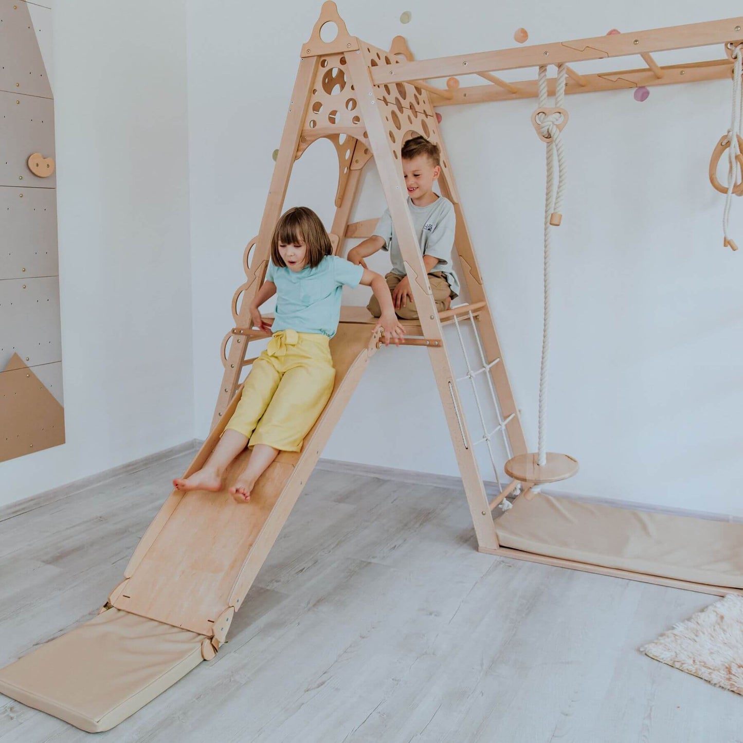 Children playing on Wood and Hearts Kid Climbing Structure in a room with white walls and light wood flooring.