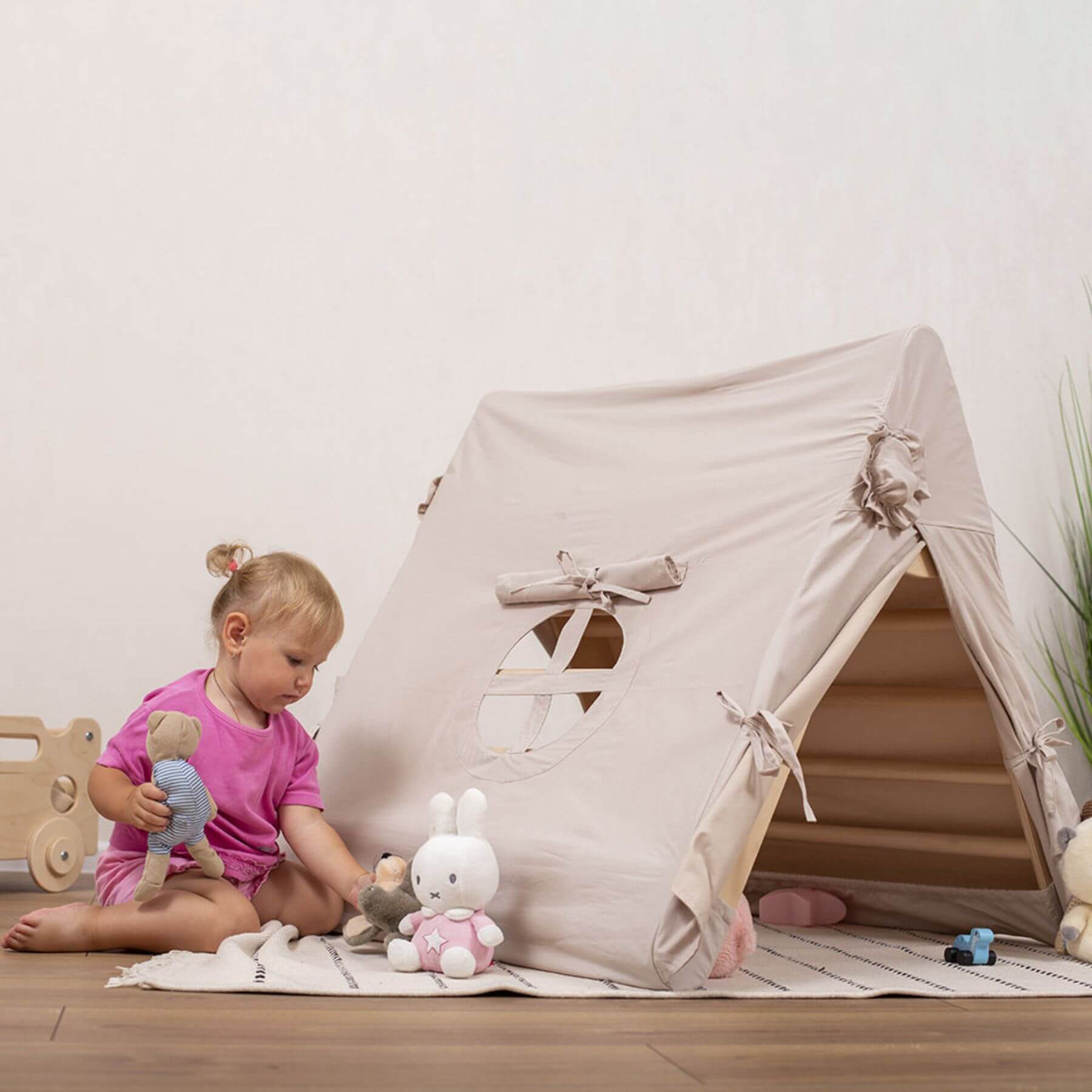 Child playing with toys in front of a beige play tent indoors.