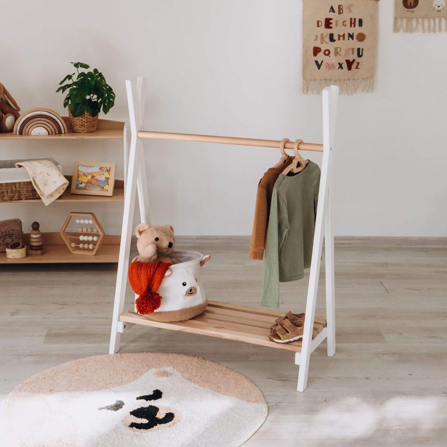 Wood and Hearts Toddler's Clothes Rack with clothes and a teddy bear in a room with shelves and decor.