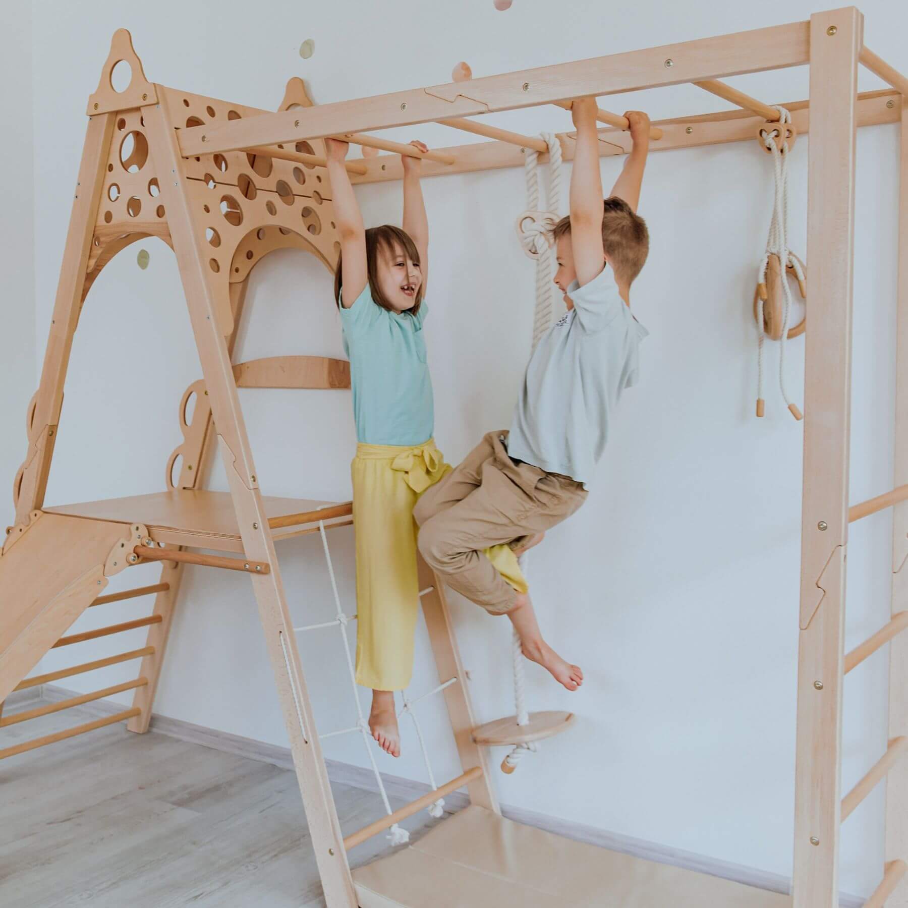 Two children playing on Wood and Hearts Wooden Playground indoors.