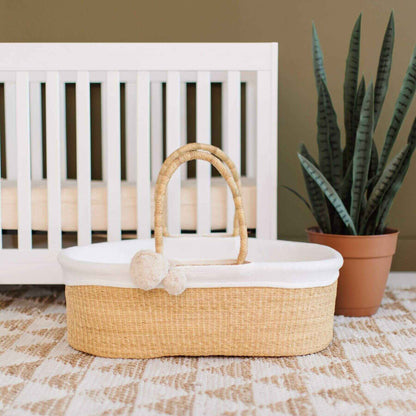 African Moses Basket No Hood Vegan Handle with white lining on a checkered floor in front of a white crib.