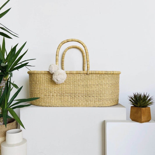 African Moses Basket No Hood Vegan Handle on a white surface with plants and a plant pot in the background