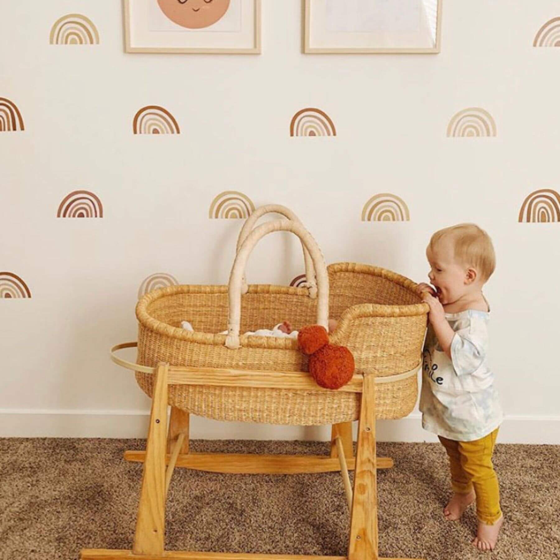 Child playing with Plum+Sparrow African Moses Basket Cream Handle in a room with rainbow wall decals.