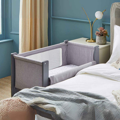 Shnuggle Air Lite Bedside Crib attached to a bed in a bedroom with blue walls and a lamp.