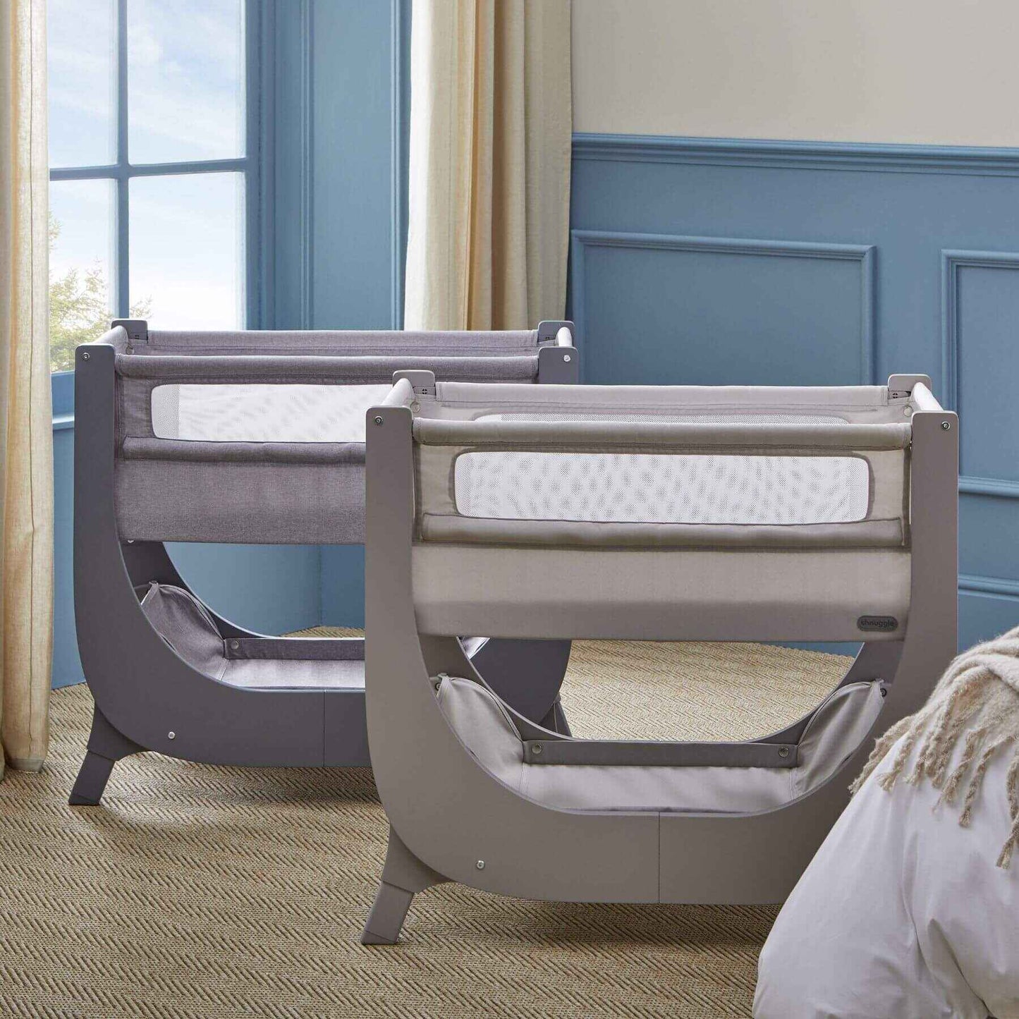 Two baby Shnuggle Air Lite Bedside Crib in a room with blue walls and a window.
