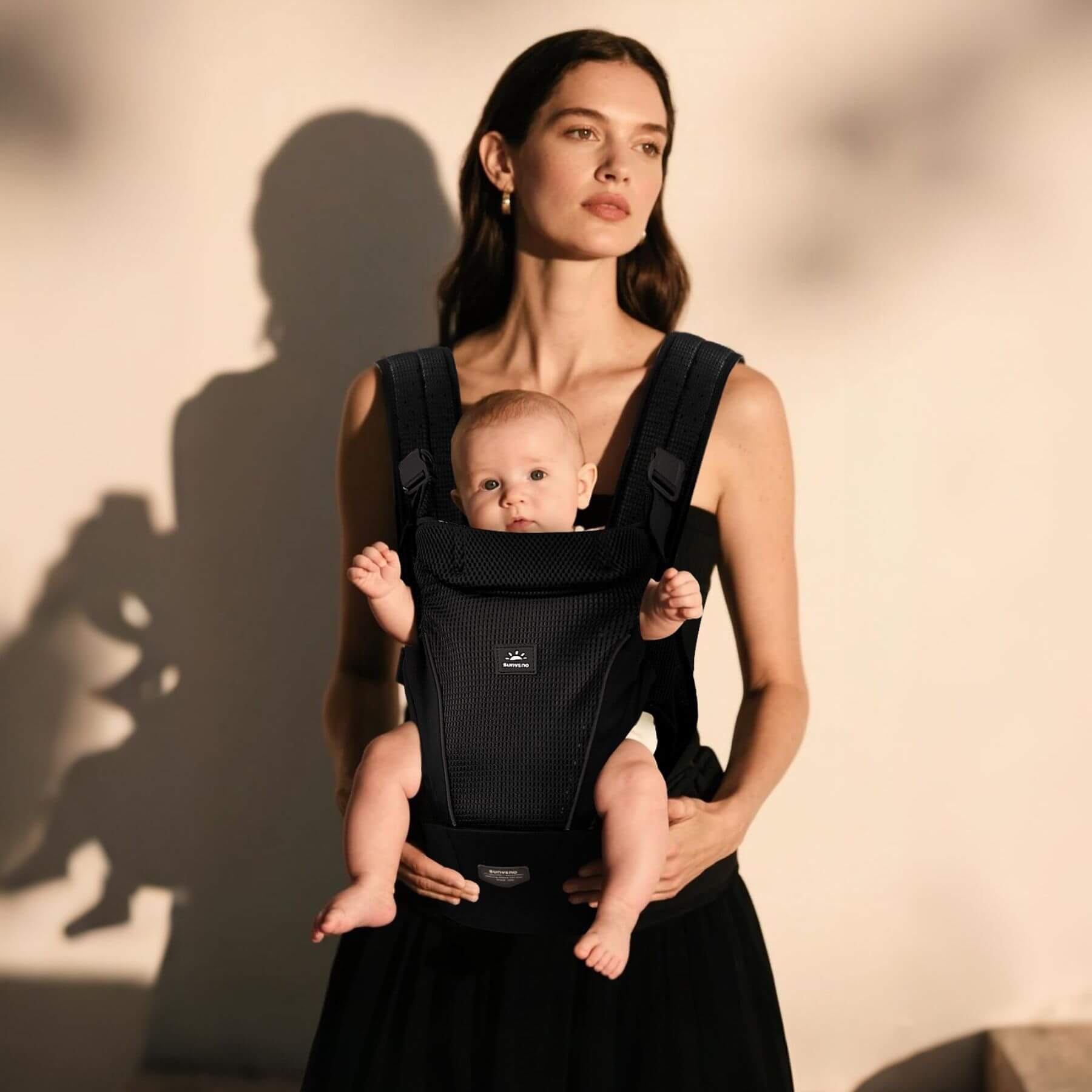 Woman holding a baby in Sunveno All-in-One Baby Carrier against a neutral background