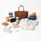 Collection of baby items including a brown bag, diapers, clothes, and accessories on a white background.