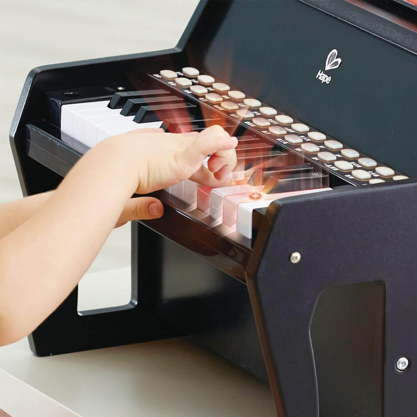 Child's hand playing a toy piano with Hape logo