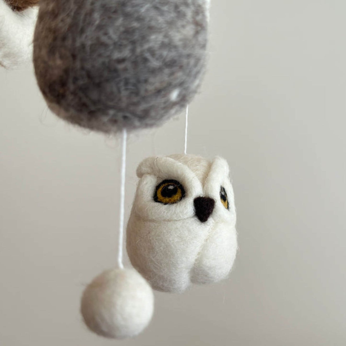 Plush owl toy hanging from a string on a plain background